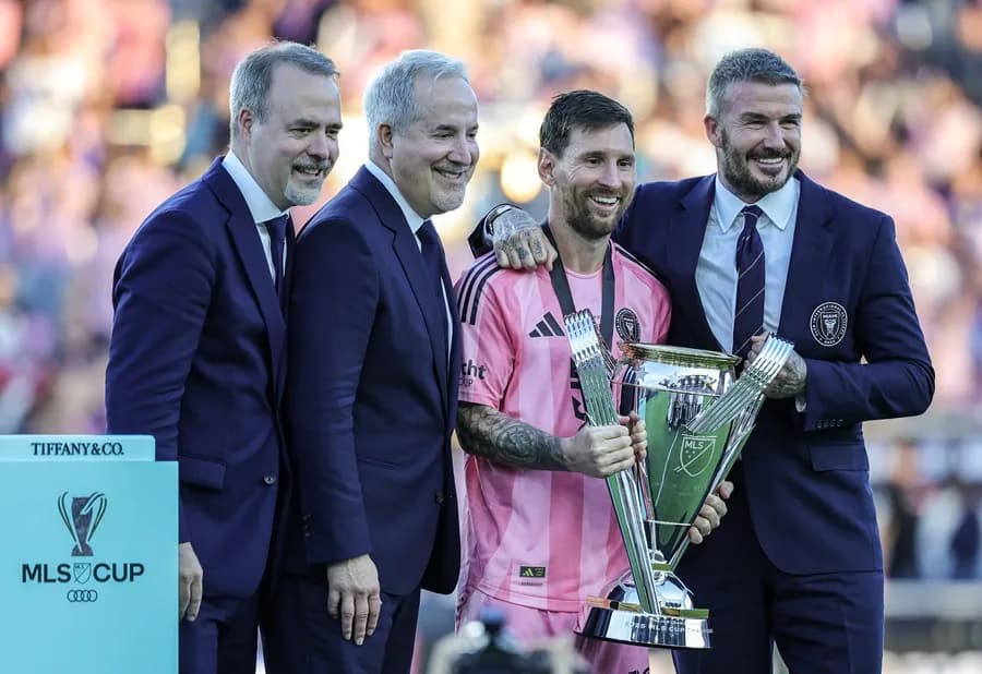 El legado de Lionel Messi ya estaba asegurado mucho antes de llegar al Inter Miami y unirse a la Major League Soccer (MLS). Había ganado una Copa del Mundo, decenas de trofeos y, en general, era considerado el mejor jugador en la historia del fútbol. No necesitaba una MLS Cup. Sin embargo, la quería, y la consiguió. Messi y el Inter Miami alcanzaron la cima, venciendo a los Vancouver Whitecaps 3-1 este sábado en la final de la MLS Cup, logrando el primer campeonato del club. Esto ocurrió dos años y medio después de la llegada de la leyenda al sur de Florida, un movimiento que sorprendió a muchos en su momento. “Decían que el fútbol nunca triunfaría en Estados Unidos”, dijo el comisionado de la MLS, Don Garber, durante la ceremonia de premiación. “Aficionados del Inter Miami, ¿ha triunfado el fútbol?” En el sur de Florida sí, gracias a Messi. Él asistió el gol que aseguró el título con un pase en el minuto 72 a Rodrigo De Paul, en una jugada donde Messi robó el balón y filtró un pase entre los defensores de Vancouver. De Paul la recibió en carrera, la mandó al rincón de la red y Messi saltó para abrazarlo unos segundos después, sonriente. Y mientras se agotaban los últimos minutos, los aficionados vestidos de rosa del Inter Miami —la mayoría con el número 10 de Messi en la espalda— se pusieron de pie y celebraron. El sur de Florida ya había visto títulos de la NFL, la NBA, la MLB y la NHL. Ahora también es una ciudad futbolera. Messi lo hizo posible. Tadeo Allende anotó en el minuto 6 del tiempo añadido —tras otra asistencia de Messi— para poner el 3-1. Y cuando Messi levantó el trofeo rodeado de sus compañeros, llovió confeti y estallaron fuegos artificiales. El Inter Miami se convirtió en la franquicia número 16 en la historia de la liga, de 30 años, en ganar un título de la MLS. Esto extiende una racha de paridad en la MLS, que ha visto a cinco franquicias diferentes ganar campeonatos en los últimos cinco años y a ocho franquicias reclamar un título en las últimas nueve temporadas; solo Columbus ha ganado dos veces en ese periodo. También fue la culminación de una odisea de 12 años para David Beckham, parte del grupo de propietarios del Inter Miami. Se retiró como jugador en 2013 y su contrato con la MLS le permitía iniciar una franquicia a tarifa reducida al terminar su carrera. Beckham eligió Miami y le tomó años hacerlo realidad; no fue hasta enero de 2018 cuando el club nació formalmente, tras asociarse con los empresarios Jorge Mas y Jose Mas, y aun así el equipo no tenía un estadio definido. El equipo comenzó a jugar en 2020, y Messi llegó a mitad de la temporada 2023. En ese momento, el Inter Miami estaba en el último lugar de la MLS. Y entonces llegó Messi. El equipo que era último, ahora lidera la liga. “Ha sido un viaje increíble”, dijo Beckham. El trofeo es el número 47 de Messi entre clubes y selección, extendiendo su récord global en el fútbol masculino, y algunos dicen que en realidad es el 48 porque la MLS otorga un trofeo por ganar el título de conferencia también. Ahora ha ganado al menos 21 títulos en finales a partido único, muchos de ellos con el núcleo de este equipo: Sergio Busquets, Jordi Alba, Luis Suárez y Javier Mascherano, sus compañeros de siempre en el Barcelona. Busquets y Alba se retiran y pudieron despedirse como campeones. El futuro de Suárez es incierto. Mascherano es ahora el entrenador, quien cambió la alineación y táctica del Inter Miami a mitad de temporada —su primera dirigiendo el club— con este momento en mente. Y el Messi de 38 años, el Jugador Más Valioso (MVP) de la MLS 2024 que parece seguro para ganar el premio otra vez esta temporada, sigue siendo único en los momentos más importantes y con un contrato que podría mantenerlo jugando en Miami hasta pasados los 40 años. Cuando comience la próxima temporada, el equipo jugará en un estadio nuevo cerca del Aeropuerto Internacional de Miami, con la mira puesta en un título consecutivo. “No está aquí solo para disfrutar de vivir en Miami”, dijo Beckham. “Su esposa y los niños aman Miami, pero él ha venido aquí para ganar, y de eso se trata realmente Leo. Quiere ganar. Tiene esa dedicación, la lealtad que muestra a sus compañeros, a la ciudad, al club. Leo es un ganador. Es así de simple”. Inter Miami se adelantó 1-0 con un autogol en el minuto ocho, antes de que Vancouver empatara en el minuto 60 con un gol de Ali Ahmed. Otro disparo de Vancouver pegó en ambos postes cerca de dos minutos después, pero no entró, y el Inter Miami recuperó la ventaja de forma definitiva cuando Messi encontró a De Paul. Y poco después del silbatazo final, Messi fue hacia la sección de aficionados del Inter Miami y levantó ambas manos en el aire. Fue un momento que se gestó durante dos años y medio.
